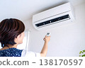 一手拿著空調遙控器調節溫度。這張圖象徵著為應對電價飆升和能源短缺而採取的措施。 138170597