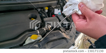 A man is checking the oil level in an internal combustion engine. Safety when going on the road. High-quality operation of the car engine. High quality photo A man is checking the oil level in an internal combustion engine. Safety when going on the road. High-quality operation of the car engine. High quality photo 138171130