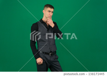 Man Thinking with Smartphone. A man in a green shirt holds a smartphone and looks up thoughtfully, against a light gray background 138171445