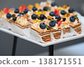 Assorted catering dessert with honey cake medovik slices topped with cream and blueberry on white buffet stand with no people and copy space 138171551