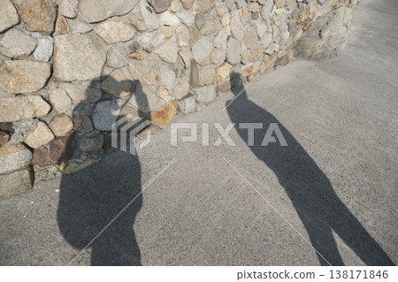 A figure's shadow reflected on a stone wall; a silhouette taking a photograph against a sunlit landscape. A figure's shadow reflected on a stone wall; a silhouette taking a photograph against a sunlit landscape. 138171846
