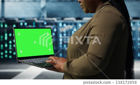 Programmer in data center using app on isolated screen laptop to ensure error free mainframes networks. Worker uses chroma key notebook to monitor server hub gear parts for failures, camera B 138172058