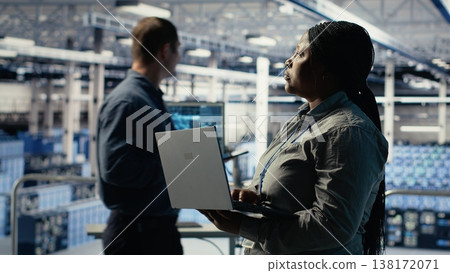 Data center admin monitors deep learning process with laptop, reviewing operational metrics. African american woman using device to review neural networks reports during inspection, camera B 138172071
