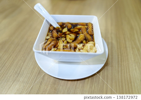 Traditional Chinese tofu pudding or Douhua served in a white bowl with ginger syrup and fried dough sticks. Delicious Asian dessert on a wooden table with a white spoon. Healthy soybean curd snack. 138172972
