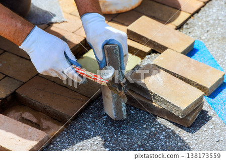 Contactor works on driveway by laying bricks using hammer to adjust their position in patio repairing surface pavement Contactor works on driveway by laying bricks using hammer to adjust their position in patio repairing surface pavement 138173559