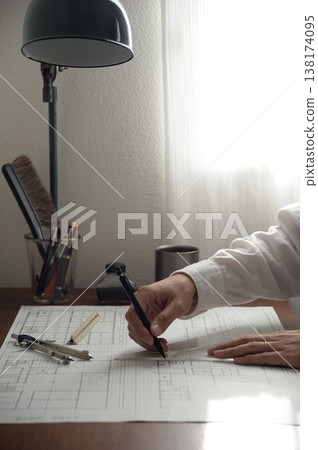 畫面中，幾隻手正在繪製建築師考試的建築圖紙，背景則是一張擺放著復古檯燈的桌子。 138174095