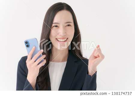 一位身穿西裝的女士面帶微笑,手裡拿著智慧型手機。 一位身穿西裝的女士面帶微笑,手裡拿著智慧型手機。 138174737