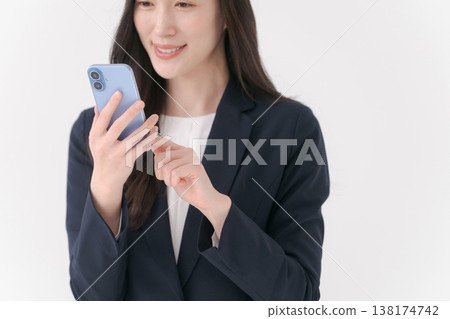 一位身穿西裝的女士面帶微笑,手裡拿著智慧型手機。 一位身穿西裝的女士面帶微笑,手裡拿著智慧型手機。 138174742