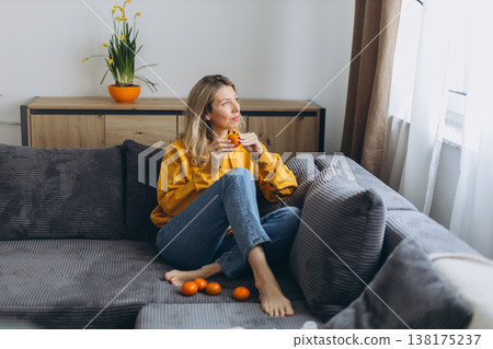 Woman eating tangerine on sofa enjoying mindful healthy lifestyle with biohacking habits and calm slow living at home Woman eating tangerine on sofa enjoying mindful healthy lifestyle with biohacking habits and calm slow living at home 138175237