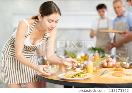 Engrossed young woman seasoning finished dish with sauce at culinary class 138175552