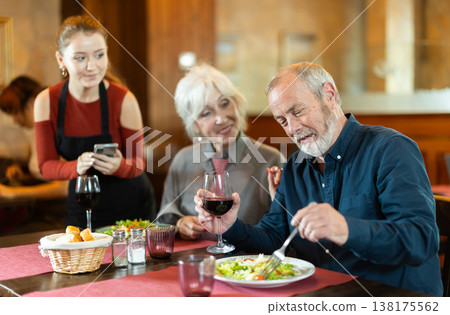 At cafe, girl waitress communicates with mature couple of customer, accepts order 138175562