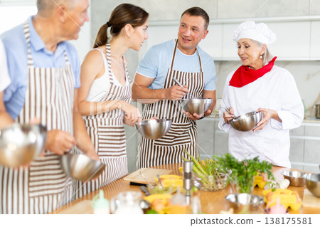 Smiling old woman chef of cooking course teaching attendees how to mix sauce 138175581
