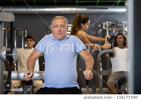 Elderly active man exercising on a simulator in modern gym 138175590