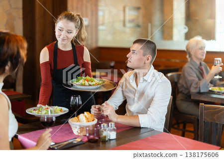 In cafe, girl waitress serves catering establishments couple visitor, puts food on table. 138175606