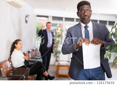 Upset adult man with documents standing in reception Upset adult man with documents standing in reception 138175639
