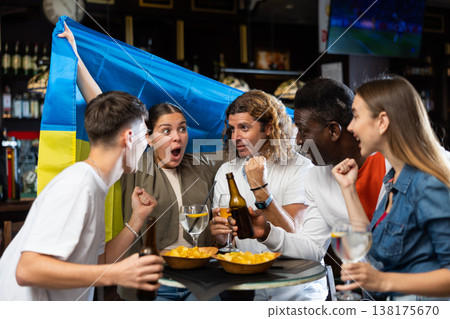 Emotional people waving flag of Ukraine while watching football match in sports pub 138175670
