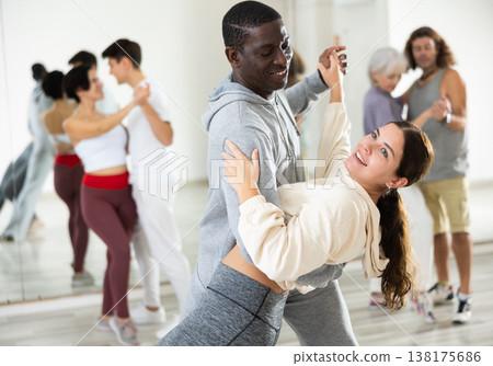 Happy african-american guy and caucasian girl practising paired latin dance in dance studio 138175686