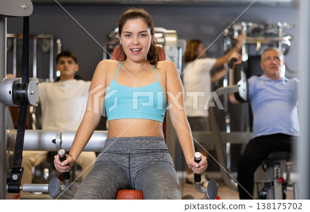 Young girl performing triceps press in exercise machine in gym 138175702