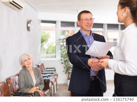 Smiling young girl makes deal, shaking hands with man colleague while standing in office. 138175740