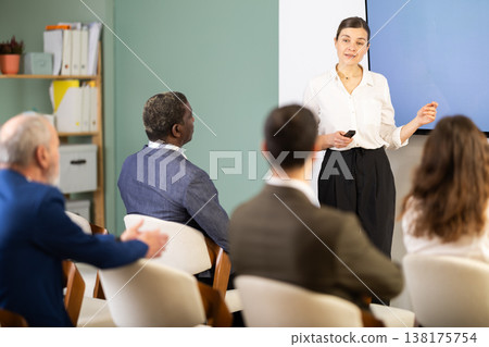 Woman lecturer with remote controller speaks to business audience of listeners, Woman lecturer with remote controller speaks to business audience of listeners, 138175754