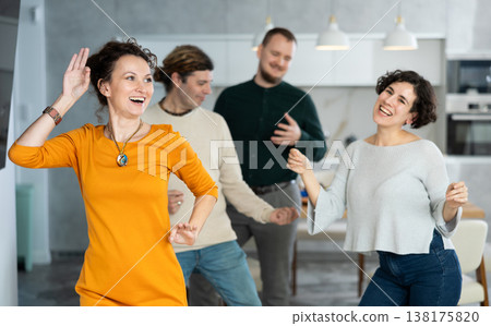 Four adult friends dancing and singing at home. Cheerful women and men enjoy music together. Happy people celebrating friendship Four adult friends dancing and singing at home. Cheerful women and men enjoy music together. Happy people celebrating friendship 138175820
