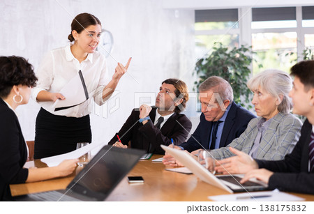 Clever young female making report while office workers of different ages using notebooks at table in office Clever young female making report while office workers of different ages using notebooks at table in office 138175832