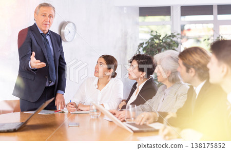 Annoyed senior male boss yelling at office colleagues of different ages taking notes at table with laptops 138175852