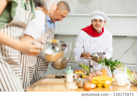 Positive young man chef of cooking course teaching attendees how to mix sauce Positive young man chef of cooking course teaching attendees how to mix sauce 138175873