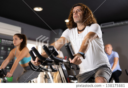 Sporty man working out on stationary bicycle in gym 138175881