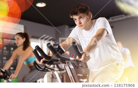 Sporty guy working out on stationary bicycle in gym Sporty guy working out on stationary bicycle in gym 138175908