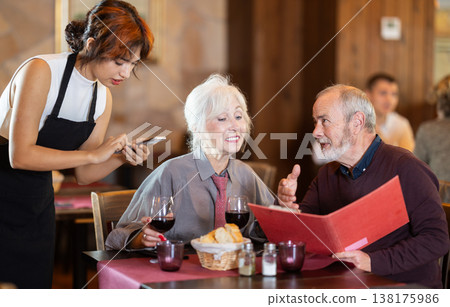 Young waitress taking order from elderly couple in restaurant Young waitress taking order from elderly couple in restaurant 138175986