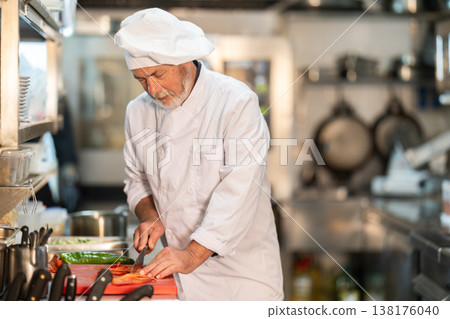 Senior man cook in kitchen finely slices food Senior man cook in kitchen finely slices food 138176040