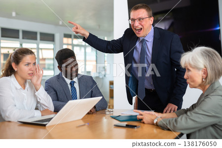 Angry middle-aged man shouting at his business partners sitting around table Angry middle-aged man shouting at his business partners sitting around table 138176050