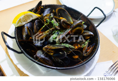 Delicious mussels on a frying pan with lemon at table Delicious mussels on a frying pan with lemon at table 138176066