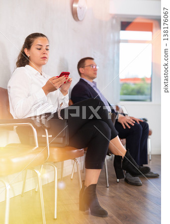 Serious-minded female candidate siting on chair and waiting for job interview in hallway Serious-minded female candidate siting on chair and waiting for job interview in hallway 138176067
