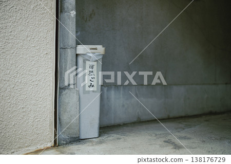 A trash can placed in a gap between buildings, with a handwritten sign indicating it's for combustible waste. A trash can placed in a gap between buildings, with a handwritten sign indicating it's for combustible waste. 138176729