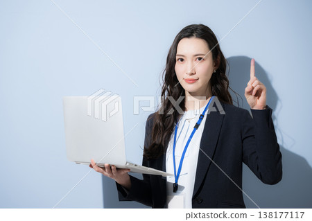 A stylish woman in a business suit with a name tag and holding a laptop is shown against a light blue background, pointing her finger while looking directly at the camera (upper body only). A stylish woman in a business suit with a name tag and holding a laptop is shown against a light blue background, pointing her finger while looking directly at the camera (upper body only). 138177117