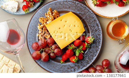 Cheese, fruits, and nuts on a table with wine glass and jar of honey at a gathering 138177661