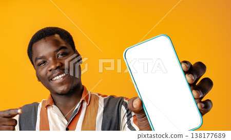 Person shows smartphone with empty screen against yellow background in studio setting 138177689