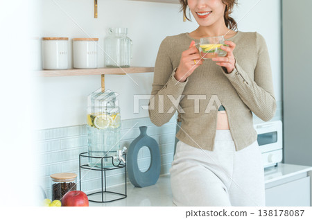 Woman drinking detox water at kitchen counter Woman drinking detox water at kitchen counter 138178087