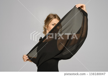 Woman holds black fabric in front of her face during indoor photo session in a studio Woman holds black fabric in front of her face during indoor photo session in a studio 138180047