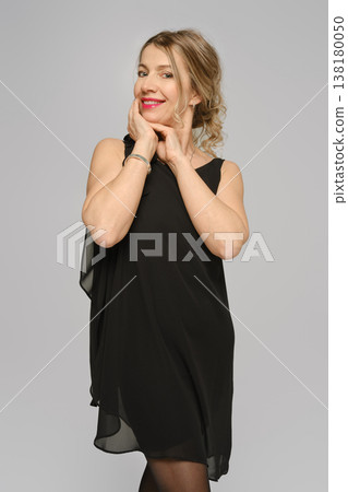 Woman posing with a cheerful expression in a simple dress against a neutral background in a studio 138180050