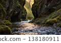 A river flows through a moss-covered canyon, sunlight filtering through narrow rock formations to create dynamic shadows on the water surface, maintaining shallow depth of field. 138180911