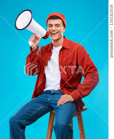 Portrait, megaphone and young man in a studio for an announcement or speech for a rally. Happy, smile and male activist on stool with bullhorn for loud communication isolated by blue background. 138182816