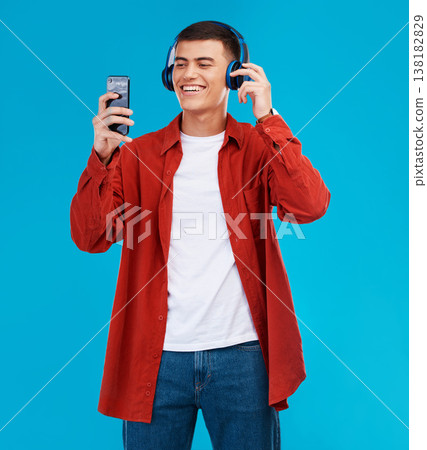 Man, smile and headphones for audio on phone in studio by blue background. Asian person, searching and streaming a song, radio and music or funny podcast on smartphone, technology and sound for joy 138182829