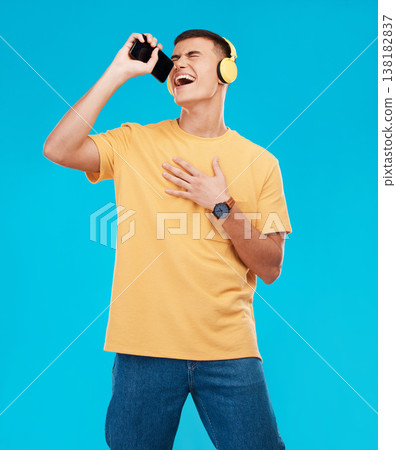 Phone, headphones and man singing in studio listening to music, radio or playlist for entertainment. Smile, technology and male person streaming song or album for karaoke isolated by blue background. Phone, headphones and man singing in studio listening to music, radio or playlist for entertainment. Smile, technology and male person streaming song or album for karaoke isolated by blue background. 138182837