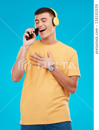 Man, headphones and singing to music with smartphone, listening to radio with karaoke on blue background. Fun, playful and entertainment with technology, audio streaming and using phone app in studio Man, headphones and singing to music with smartphone, listening to radio with karaoke on blue background. Fun, playful and entertainment with technology, audio streaming and using phone app in studio 138182839