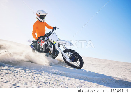 Sport, motorbike and athlete with desert with sand on wheels, pride and skill for adrenaline. Biker, sunshine and dust with blue sky in fun, fitness and achievement in speed, race or dubai vacation 138184144