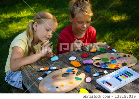 Kids carefully paint characters on rounded rocks, turning nature's canvas into charming DIY keepsakes. Kids carefully paint characters on rounded rocks, turning nature's canvas into charming DIY keepsakes. 138185039