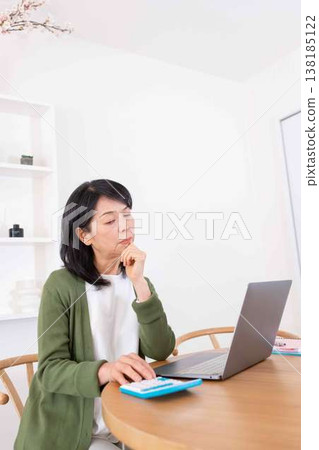 一位五十多歲的女性在使用電腦和計算器時遇到問題，正在努力解決。 138185122